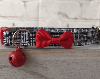 May include: A black and white plaid cat collar with a red bow tie and a red bell. The collar has a red buckle and a silver metal ring for the bell. The bell is round and shiny.