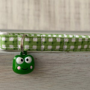 May include: Green and white gingham dog collar with a green frog charm. The frog has pink cheeks and big eyes.