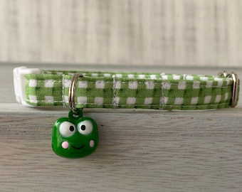 Pode incluir: Coleira de cão vichy verde e branco com um amuleto de sapo verde. O sapo tem bochechas cor-de-rosa e olhos grandes.