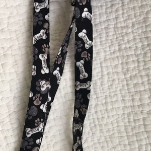 May include: Black dog leash with a pattern of paw prints and bones, with the word "BONE" printed on the bones. The leash has silver-colored bells attached to the bottom.