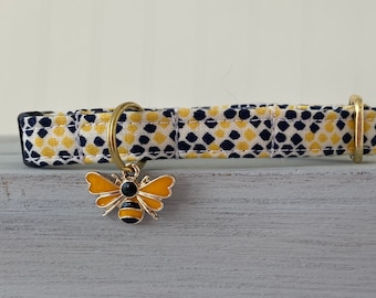 May include: A yellow and navy blue patterned fabric dog collar with a gold metal buckle and a gold bee charm.