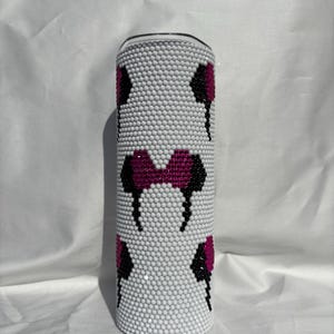 May include: A white tumbler covered in small, round, white embellishments. The tumbler features a pattern of black and magenta mouse ear designs. The top of the tumbler is silver.