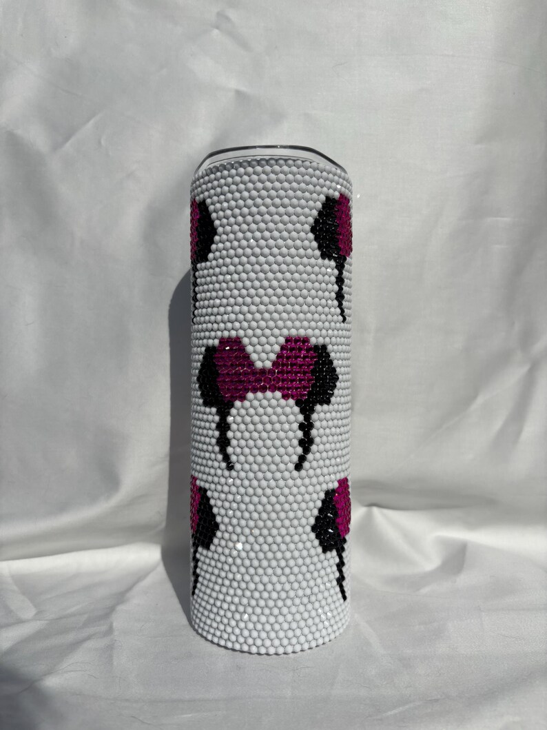 May include: A white tumbler covered in small, round, white embellishments. The tumbler features a pattern of black and magenta mouse ear designs. The top of the tumbler is silver.