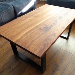 Op de afbeelding: Een houten salontafel met een natuurlijke houten afwerking en een zwart metalen frame. De tafel staat op een hardhouten vloer.