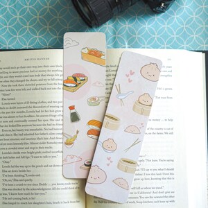 May include: Two decorative bookmarks with a food theme. One features sushi and soy sauce illustrations, the other has dumpling and chopstick designs. Both are light-colored with rounded corners, perfect for book lovers.