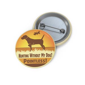 May include: A round button with a brown dog silhouette on an orange and yellow background. The text reads "Hunting Without My Dog? Pointless!" The button has a metal pin back and a cream-colored border.