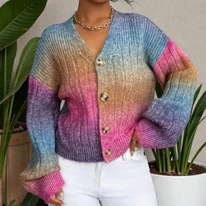 May include: A multi-coloured button-down cardigan in a rainbow gradient, featuring shades of blue, pink, orange, and purple. The V-neck sweater has a ribbed texture and gold-toned buttons. The long-sleeved garment has a casual style.