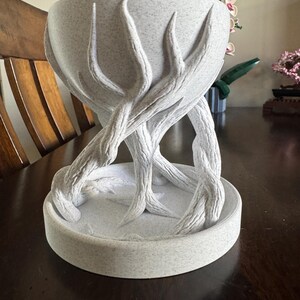 May include: A light grey decorative bowl with a textured surface, supported by stylized branches. The bowl has a rounded shape and sits on a circular base. The branches are intricately designed, adding a naturalistic touch to the piece.