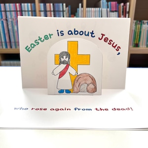 May include: A colourful card with a pop-up illustration of Jesus standing next to a tomb. The card reads "Easter is about Jesus, who rose again from the dead!"