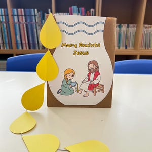 以下が含まれることがあります： 「Mary Anoints Jesus」のテキストが入った、聖書のシーンを描いた手作りのクラフト。 マリアとイエスのイラストと、黄色の涙型の切り抜きが含まれています。 クラフトは図書館を背景にしています。