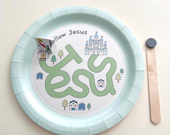 May include: A light blue paper plate with a printed maze that spells "Jesus" in green. The maze features a castle, houses, and trees. A small flag and a wooden stick with a black magnet are also present.