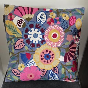 May include: A gray throw pillow with a floral embroidery design. The flowers are pink, yellow, blue, and red. The pillow is made of a soft, comfortable fabric.