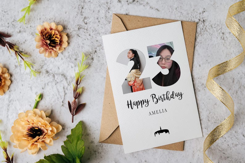 K&ouml;nnte beinhalten: Eine wei&szlig;e Geburtstagskarte mit der Zahl 23, die Fotoausschnitte einer Person enth&auml;lt, sowie dem Text Happy Birthday und AMELIA und einem kleinen schwarzen Kuchen-Symbol. Die Karte liegt auf einem braunen Umschlag mit pfirsichfarbenen Blumen.