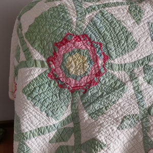 May include: A white quilt with a green and pink floral pattern. The quilt is quilted with a diamond pattern. The quilt is made of cotton fabric.