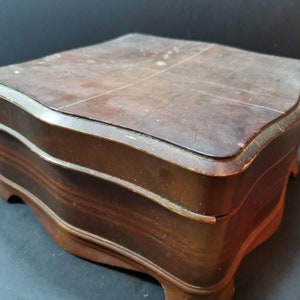 Puede incluir: Una caja de madera con un acabado marr&oacute;n oscuro y un borde festoneado. La caja tiene una tapa con bisagras y se asienta sobre cuatro patas.
