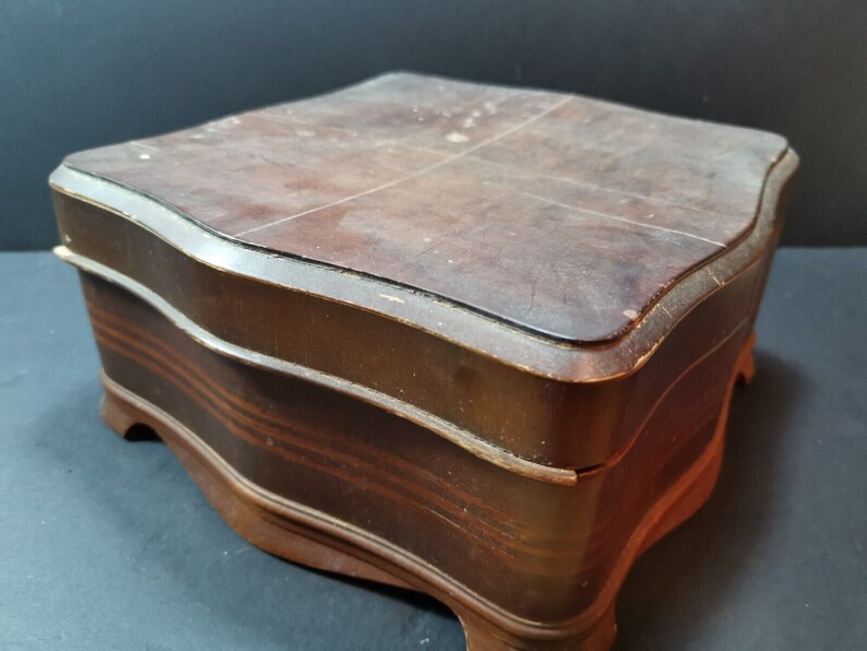 Puede incluir: Una caja de madera con un acabado marr&oacute;n oscuro y un borde festoneado. La caja tiene una tapa con bisagras y se asienta sobre cuatro patas.