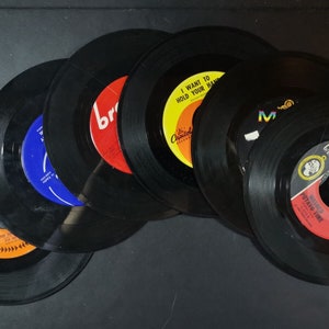 May include: A stack of six black vinyl records with colorful labels. The labels feature text such as "I Want to Hold Your Hand" and "Potato Time".