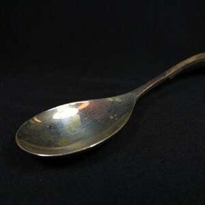 May include: A silver spoon with a curved handle. The spoon has a shiny, reflective surface with some minor scratches.