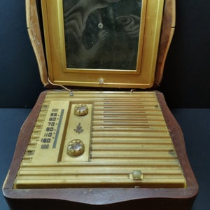 Puede incluir: Una radio vintage de madera con un panel frontal dorado y una ventana de vidrio en la parte superior. La radio tiene un dial con n&uacute;meros del 55 al 160 y dos perillas. La radio est&aacute; en una caja de madera con un acabado marr&oacute;n oscuro.