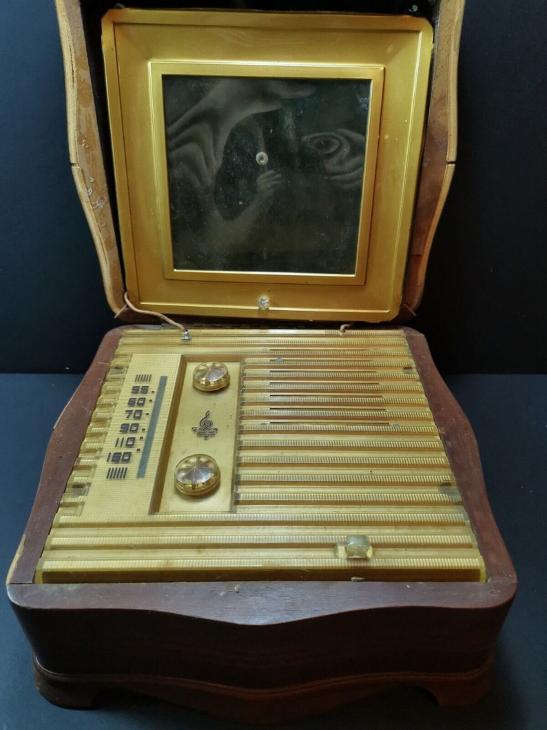 Puede incluir: Una radio vintage de madera con un panel frontal dorado y una ventana de vidrio en la parte superior. La radio tiene un dial con n&uacute;meros del 55 al 160 y dos perillas. La radio est&aacute; en una caja de madera con un acabado marr&oacute;n oscuro.
