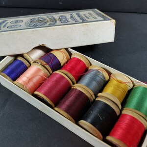May include: A box of assorted thread spools in a variety of colors, including red, green, blue, purple, and yellow. The spools are made of wood and have a white label with black text. The box is made of cardboard and has a white label with black text. The text on the label reads "The Anchor Thread Co. Ltd.  Made in England."
