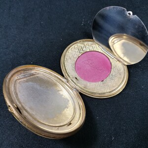 May include: A vintage gold compact with a hinged mirror and a red blush refill. The blush refill has the word "Blush" written on it.