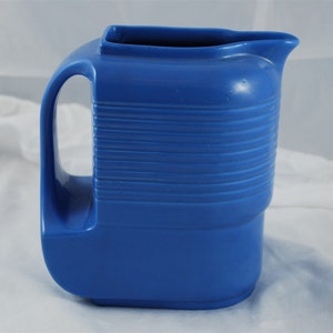 May include: A blue ceramic pitcher with a ribbed design. The pitcher has a wide mouth and a handle.