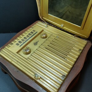 Puede incluir: Una radio vintage de madera con un panel frontal dorado y una tapa de espejo. La radio tiene un dial con n&uacute;meros y algunas perillas. La radio est&aacute; en posici&oacute;n cerrada.