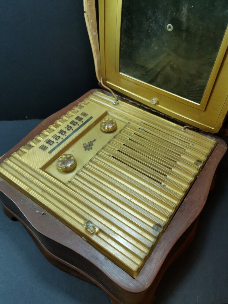 Puede incluir: Una radio vintage de madera con un panel frontal dorado y una tapa de espejo. La radio tiene un dial con n&uacute;meros y algunas perillas. La radio est&aacute; en posici&oacute;n cerrada.
