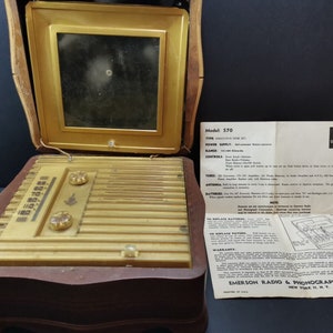 Puede incluir: Un radio-fon&oacute;grafo combinado Emerson modelo 370 vintage en una caja de madera. La radio tiene un panel frontal de color dorado con un dial, dos botones y una rejilla de altavoz. El fon&oacute;grafo est&aacute; en el compartimento superior y tiene una peque&ntilde;a ventana cuadrada. La radio viene acompa&ntilde;ada de un manual de instrucciones.