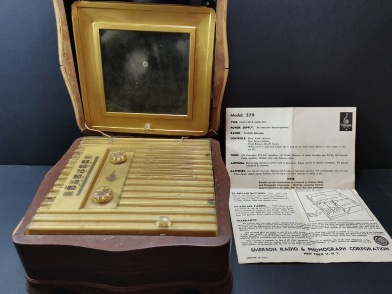 Puede incluir: Un radio-fon&oacute;grafo combinado Emerson modelo 370 vintage en una caja de madera. La radio tiene un panel frontal de color dorado con un dial, dos botones y una rejilla de altavoz. El fon&oacute;grafo est&aacute; en el compartimento superior y tiene una peque&ntilde;a ventana cuadrada. La radio viene acompa&ntilde;ada de un manual de instrucciones.