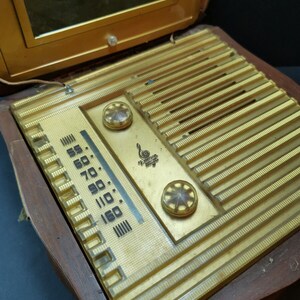 Puede incluir: Una radio vintage de madera con una cara dorada y un dial de pl&aacute;stico transparente. La radio tiene un espejo en la parte superior y una perilla en el lado derecho. El dial tiene n&uacute;meros del 55 al 160.
