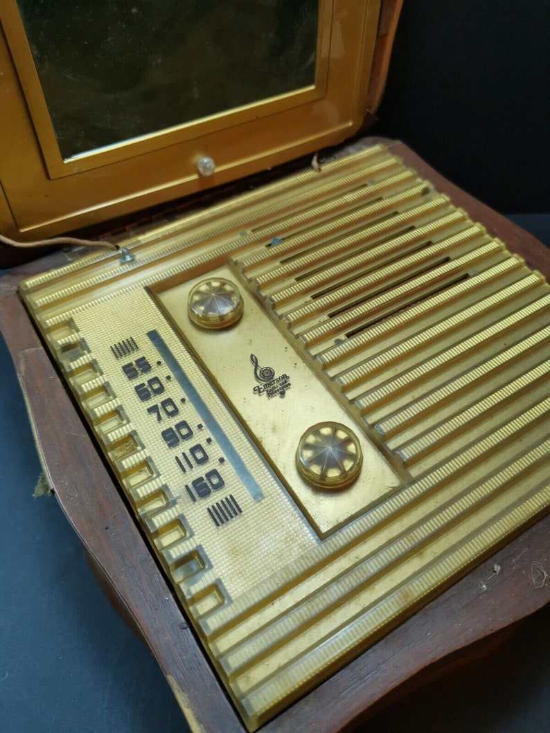 Puede incluir: Una radio vintage de madera con una cara dorada y un dial de pl&aacute;stico transparente. La radio tiene un espejo en la parte superior y una perilla en el lado derecho. El dial tiene n&uacute;meros del 55 al 160.