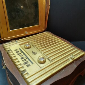 Puede incluir: Una radio vintage de madera con un panel frontal dorado y un altavoz negro. La radio tiene un dial con n&uacute;meros del 55 al 160 y dos botones. La radio est&aacute; abierta y el altavoz es visible.