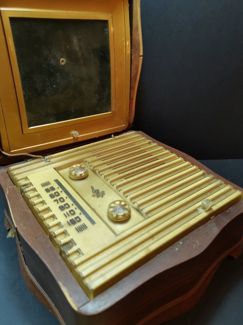 Puede incluir: Una radio vintage de madera con un panel frontal dorado y un altavoz negro. La radio tiene un dial con n&uacute;meros del 55 al 160 y dos botones. La radio est&aacute; abierta y el altavoz es visible.