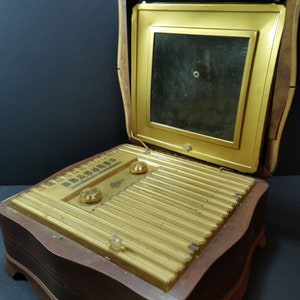 Puede incluir: Una radio vintage de madera con un panel frontal dorado y una peque&ntilde;a pantalla. La radio est&aacute; abierta y la pantalla es visible. La radio tiene un dise&ntilde;o decorativo y est&aacute; en buen estado.
