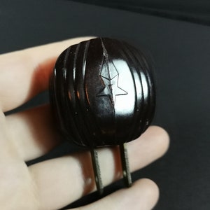May include: A black bakelite electrical plug with two prongs and a star-shaped design.
