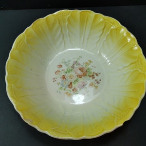 May include: A white ceramic bowl with a yellow rim and floral design. The bowl has a scalloped edge and a raised design on the rim.