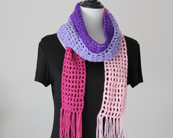 May include: A handmade crochet scarf in shades of purple, lavender, and pink. The scarf is draped on a black mannequin, showcasing its open weave design and fringed ends. The scarf is a stylish accessory.