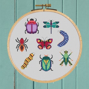 Könnte beinhalten: Ein Kreuzstich-Stickrahmen mit weißem Hintergrund und bunten Bildern verschiedener Insekten, darunter ein Schmetterling, ein Marienkäfer, eine Libelle, eine Raupe und eine Spinne.