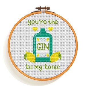 Könnte beinhalten: Stickrahmen mit Kreuzstich-Stickerei auf weißem Hintergrund und dem Text "You're the gin to my tonic". Das Design zeigt eine grüne Gin-Flasche mit einem weißen Etikett, auf dem "GIN" steht, und zwei gelbe Zitronen.