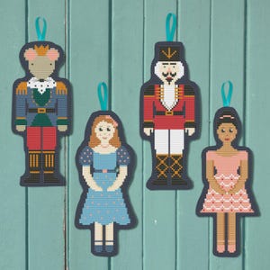 May include: Four felt ornaments featuring characters from the Nutcracker ballet. A mouse wearing a blue and green uniform, a soldier in a red and white uniform, a girl in a blue dress, and a ballerina in a pink dress.