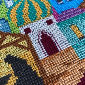 Peut inclure: Gros plan sur une broderie au point de croix color&eacute;e repr&eacute;sentant une ville avec des b&acirc;timents, un d&ocirc;me et une vari&eacute;t&eacute; de couleurs, notamment le vert, le jaune, le bleu, le violet et le marron.