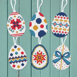 May include: Six colorful Easter eggs with different geometric patterns. The eggs are white with red, blue, yellow, and gold accents. The eggs are hanging from a white string.