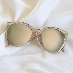 May include: A pair of tortoise shell sunglasses with mirrored lenses. The sunglasses are lying on a white fabric surface.