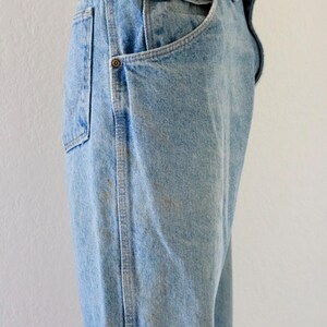 May include: Light blue denim jeans with a classic five-pocket design. The jeans have a high waist and a straight leg cut. Features include metal rivets and a brown leather belt loop. The denim has a faded wash with subtle wear marks.