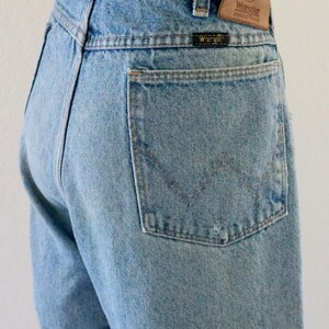 May include: Light blue denim jeans with a classic five-pocket design. The jeans feature a Wrangler brand patch on the back waistband and a small Wrangler label on the back pocket. The jeans are a light wash and have a straight leg.