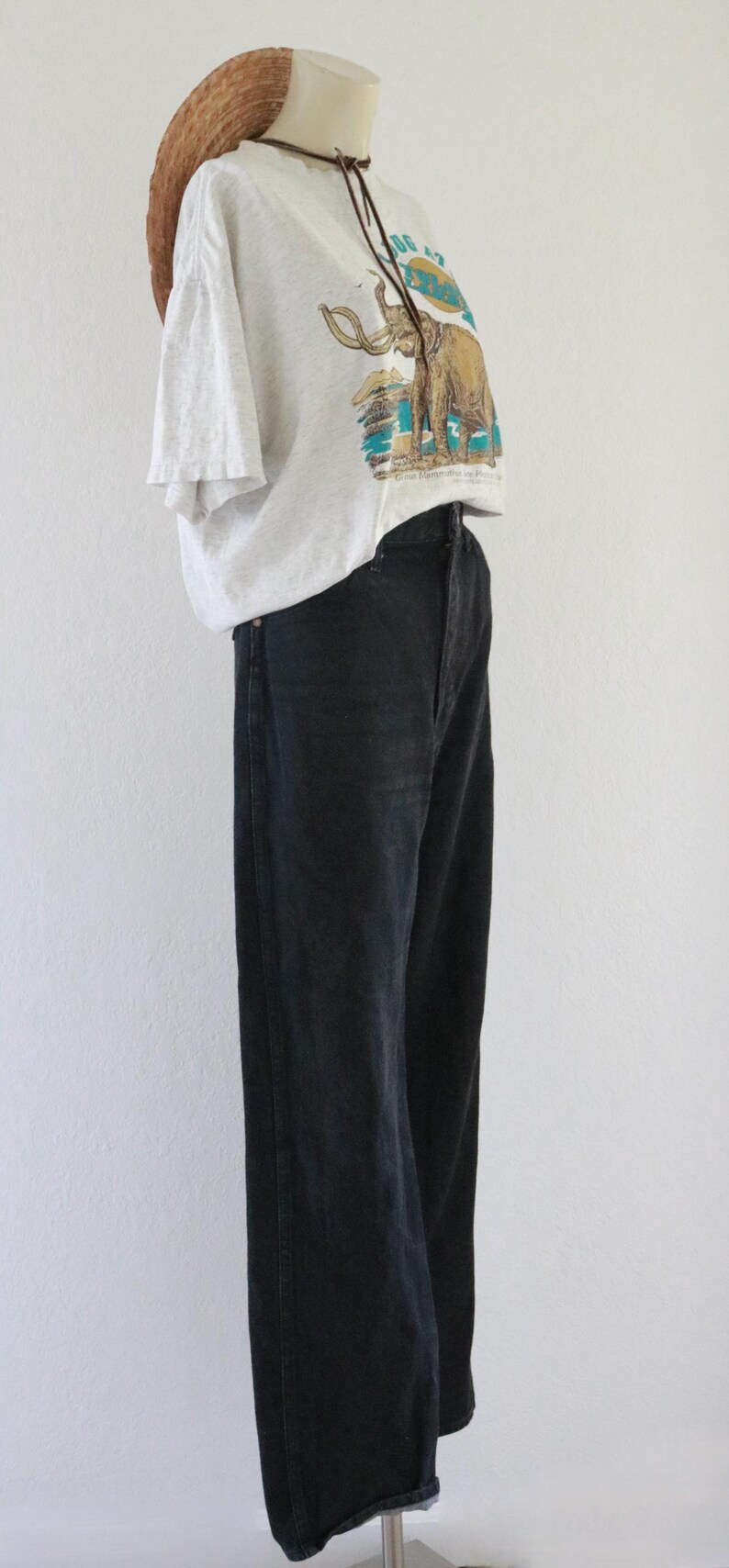 Puede incluir: Una camiseta gris claro con un gr&aacute;fico de mamut, combinada con vaqueros negros y un sombrero de paja. El conjunto se exhibe en un maniqu&iacute;, mostrando un estilo casual y vintage.
