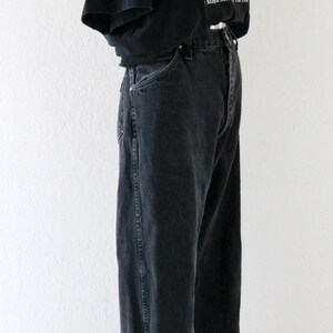 May include: A black t-shirt with a graphic design and the text "Maya Meet 199". The shirt is paired with black denim jeans and a straw hat. The outfit is displayed on a mannequin against a white background.