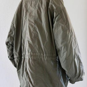 Pu&ograve; includere: Giacca parka verde oliva con vita regolabile con coulisse e collo alto. La giacca ha una vestibilit&agrave; ampia e maniche lunghe. Vista posteriore che mostra i dettagli delle cuciture. Capo di abbigliamento classico.